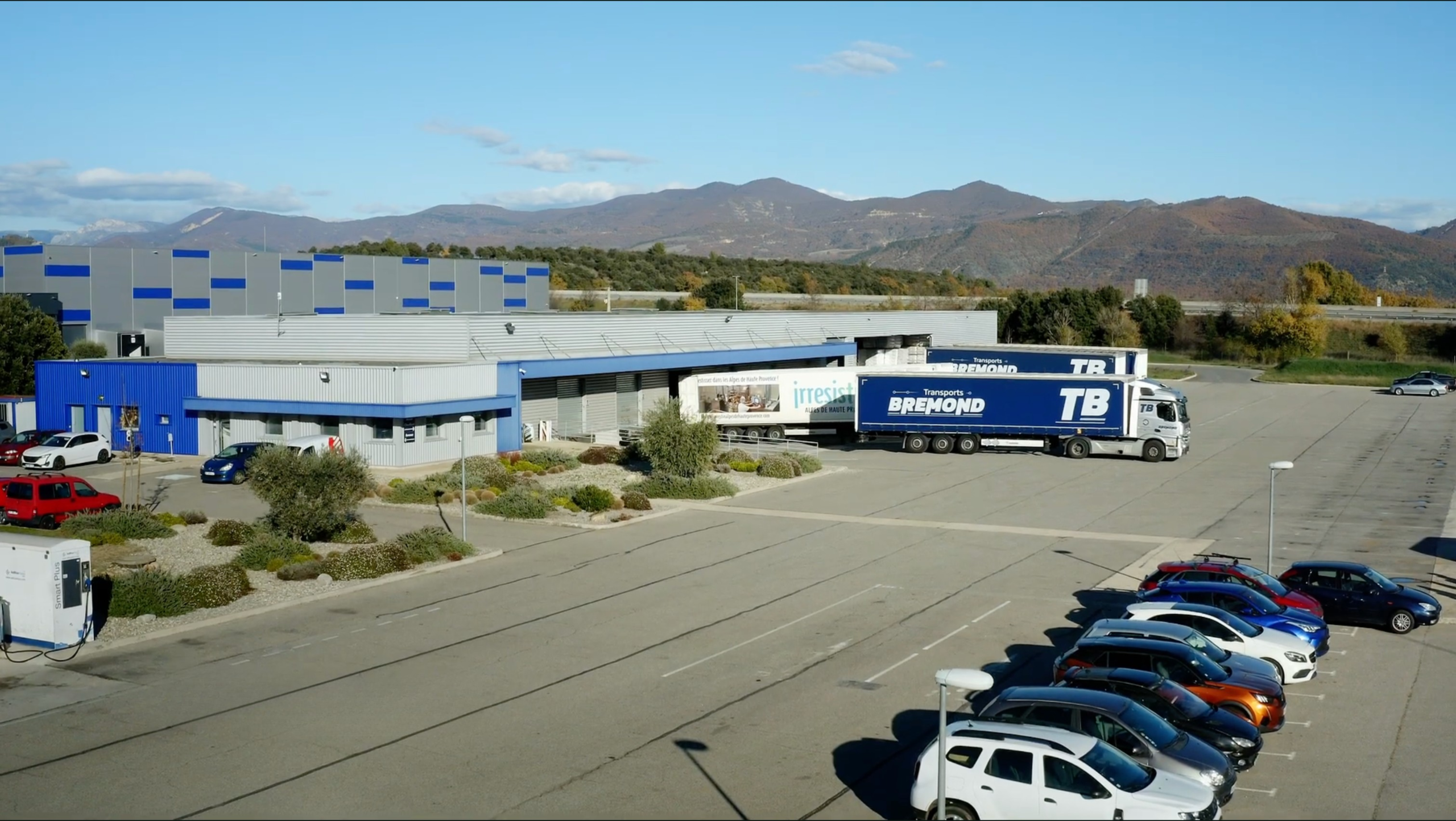 Site logistique des Transports Brémond avec deux ensembles articulés à quai et un parking, au pied des montagnes des Alpes-de-Haute-Provence